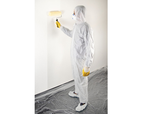 Person mit Schutzanzug streicht Wand mit Farbroller