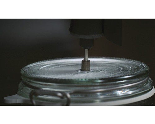 Ein Werkzeug bohrt ein Loch in den Deckel eines Einmachglases.