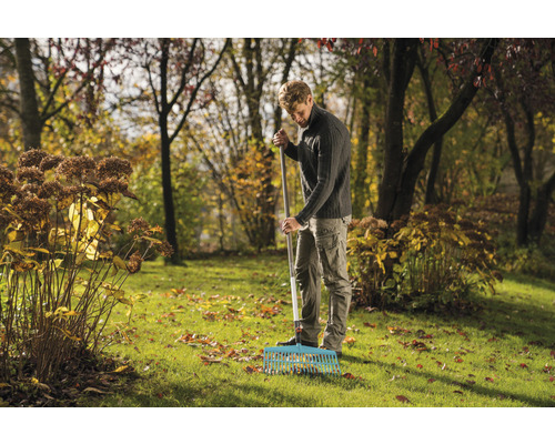 Ein Mann kehrt mit einem Rechen Laub in einem Garten.