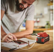Ein Mann lädt sein Mobiltelefon mit einem Akku-Adapter auf einer Werkbank.
