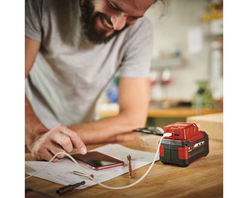 Ein Mann lädt sein Mobiltelefon mit einem Akku-Adapter auf einer Werkbank.
