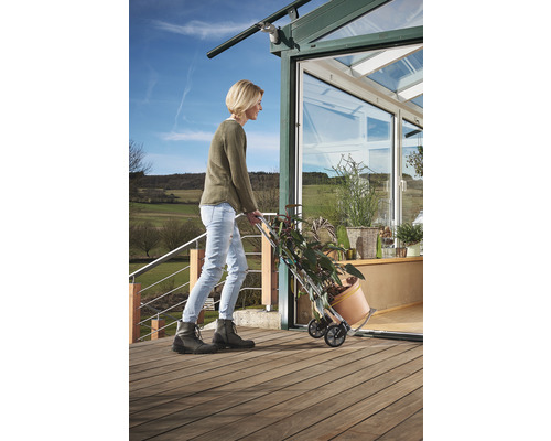 Frau transportiert Pflanzen mit einer Sackkarre vor ein Gewächshaus.