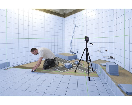Ein Mann verlegt Fliesen in einem Badezimmer, wobei ein Laser-Nivelliergerät verwendet wird, um die Ausrichtung zu gewährleisten.