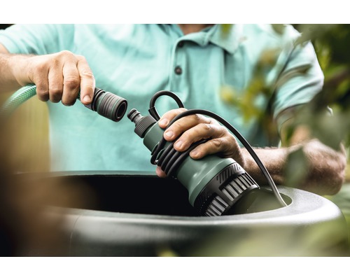 Mann schliesst Regenfasspumpe an Gartenschlauch an