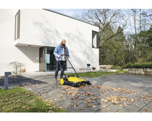 Mann kehrt Laub mit einer Kehrmaschine vor einem Wohnhaus.