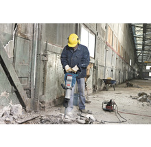 Bauarbeiter mit Presslufthammer bei Abbrucharbeiten in einem Gebäude.