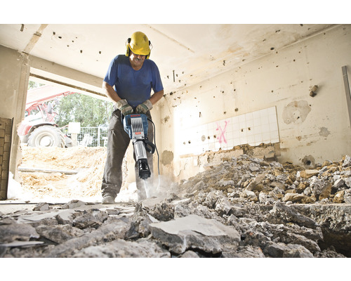 Ein Bauarbeiter benutzt einen Bohrhammer zum Abbruch von Mauerwerk in einem Raum.
