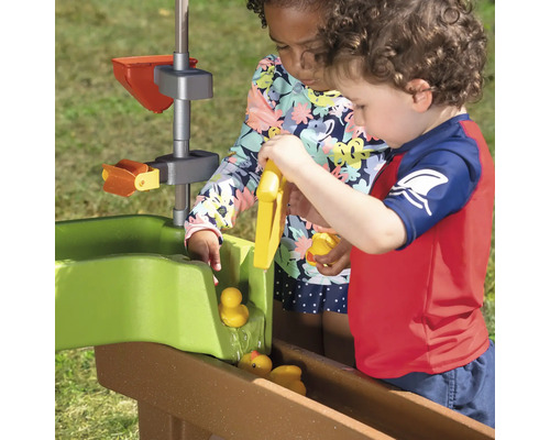 Zwei Kinder spielen mit einem Wasserbahnsystem und Spielzeugenten im Freien.