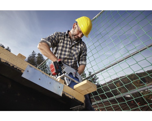 Ein Mann mit Schutzhelm sägt ein Holzbrett mit einer Bosch Kreissäge auf einem Dach.