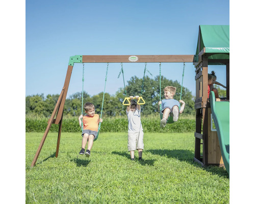Kinder spielen auf einem Spielplatz mit Schaukeln, Turnringen, Rutsche und Spielhaus.