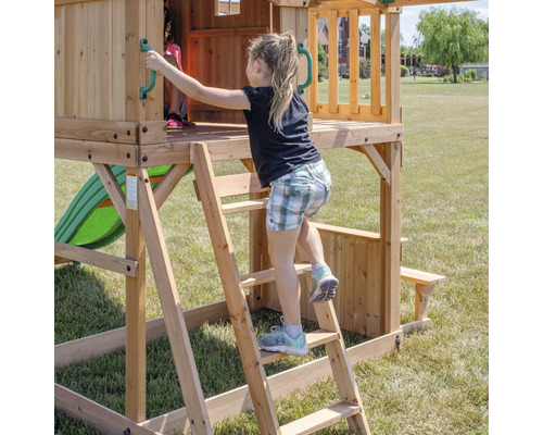 Mädchen klettert auf einem Holzspielturm mit Rutsche und Picknicktisch