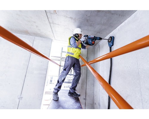 Ein Bauarbeiter bohrt mit einem Bohrhammer ein Loch in eine Betonwand.