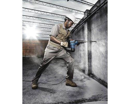 Ein Bauarbeiter bohrt mit einem Bohrhammer ein Loch in eine Betonwand.