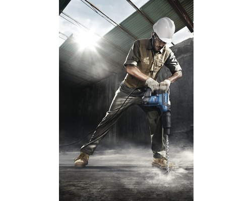 Ein Bauarbeiter mit Schutzhelm bohrt mit einem Bohrhammer in den Boden.