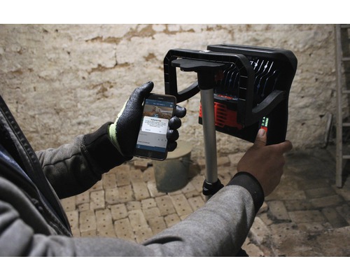 Arbeiter bedient LED-Baustrahler mit Smartphone-App.