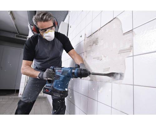Mann arbeitet mit einem Bohrhammer an einer Wand mit Fliesen.