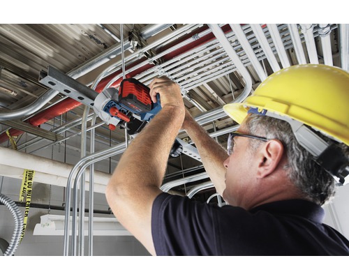Ein Mann mit Schutzhelm schneidet mit einer Rohrsäge ein Metallrohr an einer Decke.