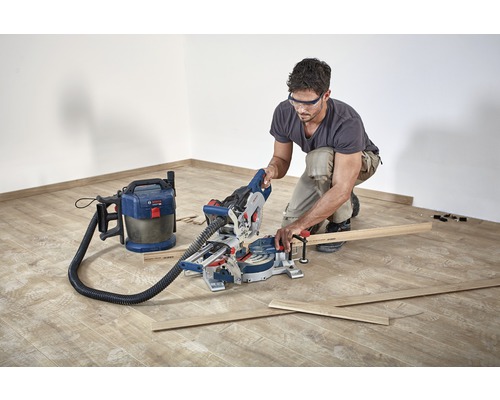 Mann arbeitet mit einer Kappsäge und einem Staubsauger auf einem Holzboden.