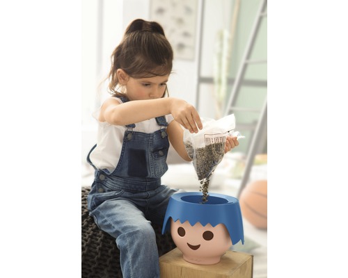 Ein Mädchen schüttet Samen in einen Pflanztopf mit Gesicht