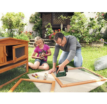 Vater und Tochter bauen einen Hasenstall im Garten mit einem Tacker, Holz und Drahtgitter.