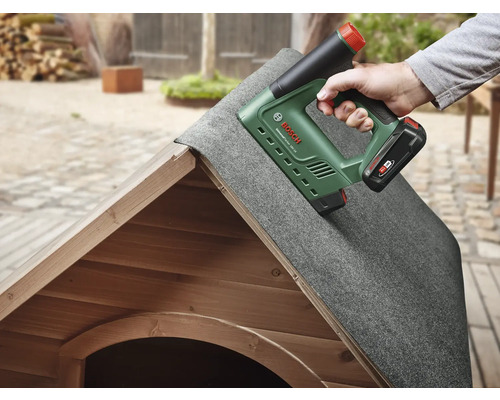 Eine Person befestigt Dachpappe mit einem Akku-Tacker auf einem Holzhaus.