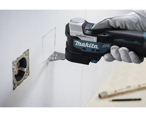 Makita Multifunktionswerkzeug schneidet eine Öffnung in eine Wand neben einer Steckdose.