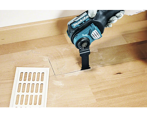 Makita Multifunktionswerkzeug im Einsatz auf Holzboden neben einem Lüftungsgitter.