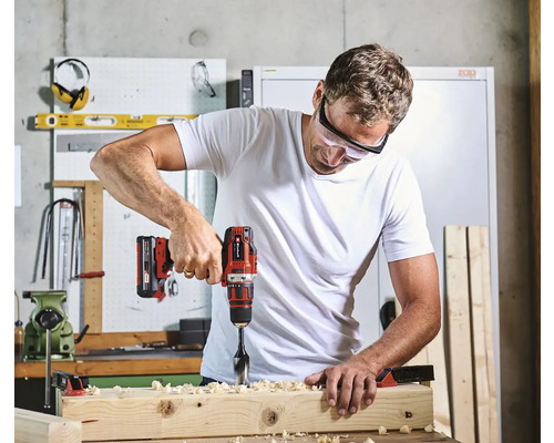 Ein Mann bohrt mit einer Bohrmaschine ein Loch in ein Holzbrett.