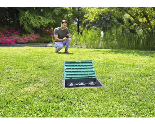 Garten mit Bewässerungssystem und Mann mit Mobiltelefon