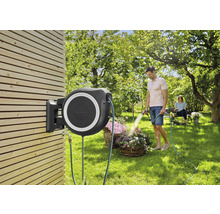 Gartenszene mit an einer Holzwand montierter Schlauchbox und Mann, der Blumen gießt