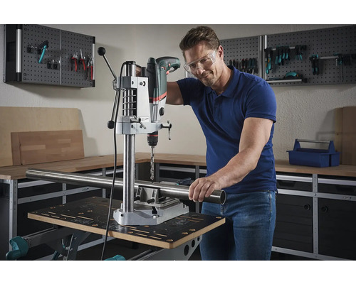 Mann bohrt mit einer Tischbohrmaschine ein Rohr in einer Werkstatt.
