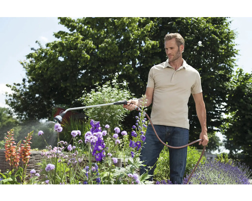 Mann bewässert Blumen mit einer Gartenspritze im Garten.