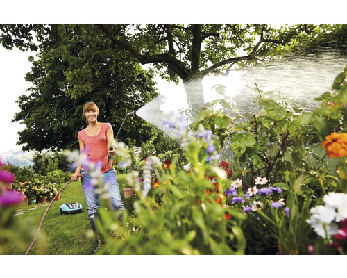 Frau bewässert Pflanzen im Garten mit Gartenschlauch