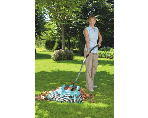 Frau rechen Laub mit einem Gartenrechen im Garten.