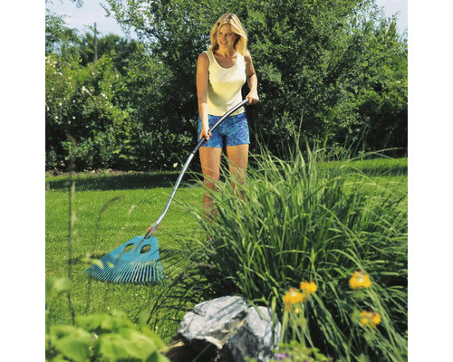 Eine Frau benutzt einen Fächerbesen im Garten, um Blätter und Gartenabfälle zu entfernen.