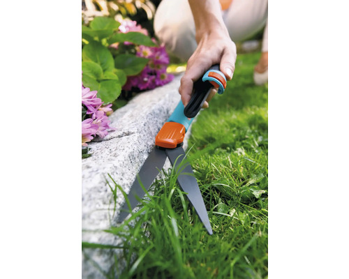 Person schneidet Gras mit einer Rasenkantenschere entlang eines Steins