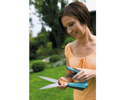 Frau betrachtet Grasschere vor Gartenkulisse