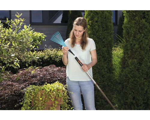 Frau befestigt einen Rechenkopf an einem Stiel im Garten.