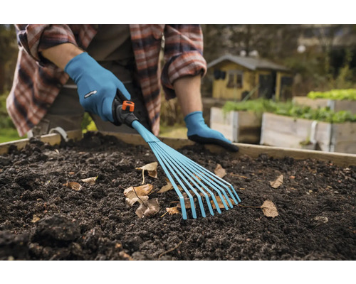 Eine Person harkt mit einem Gardena Rechen Laub in einem Hochbeet.