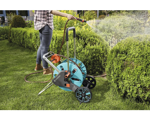 Frau gießt Garten mit Gartenschlauchwagen und Schlauch