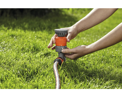 Person stellt einen Rasensprenger auf dem Rasen ein.