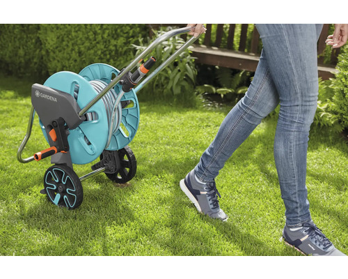 Gartenszene mit einer Person, die einen Gardena Schlauchwagen über einen Rasen zieht.