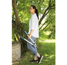 Eine Frau steht im Garten und hält eine Astschere in der Hand.