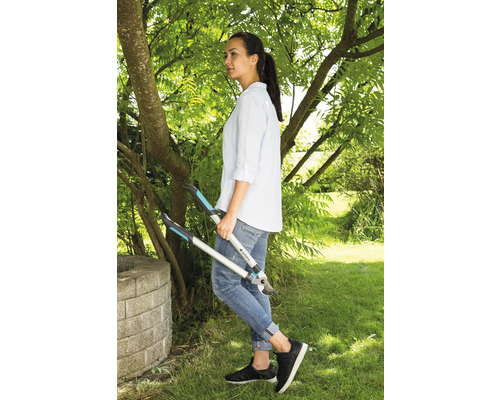 Eine Frau steht im Garten und hält eine Astschere in der Hand.