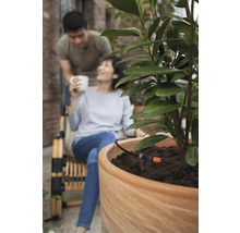 Automatische Bewässerung in einem Blumentopf auf einer Terrasse mit Paar im Hintergrund.