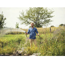 Mann bewässert Garten mit Gartenschlauch und Spritzpistole