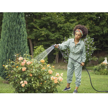 Eine Frau gießt Rosen mit einem Gartenschlauch im Garten.