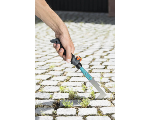 Hand hält einen Fugenkratzer zum Entfernen von Unkraut zwischen Pflastersteinen.