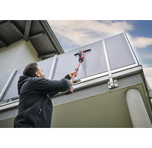 Mann reinigt Glasbrüstung mit einem Akku-Fensterreiniger.