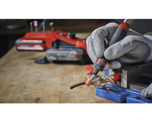 Person schleift Metall mit einem Multifunktionswerkzeug und Schutzhandschuhen in einer Werkstatt.